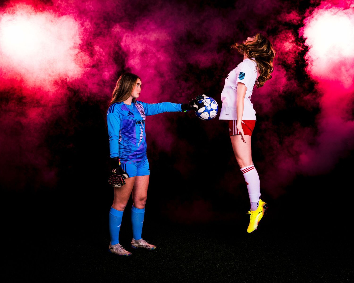 Soccer players in blue and white uniforms jump to head the ball during a match with pink smoke in the background.