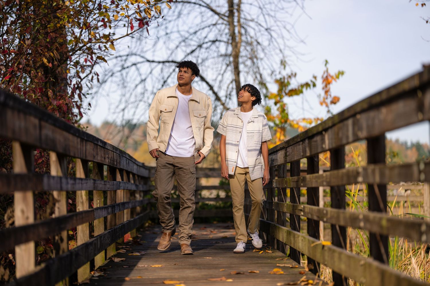 Couple in white outfits walking hand in hand across a wooden bridge during golden hour.