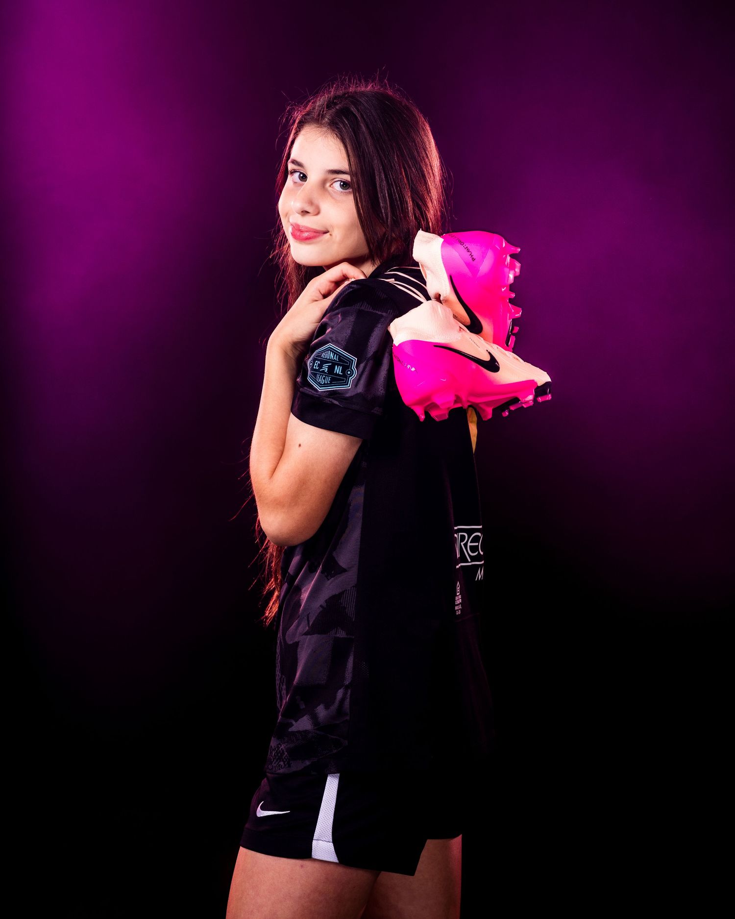 Athlete in dark sportswear holds pink gear against purple backdrop.