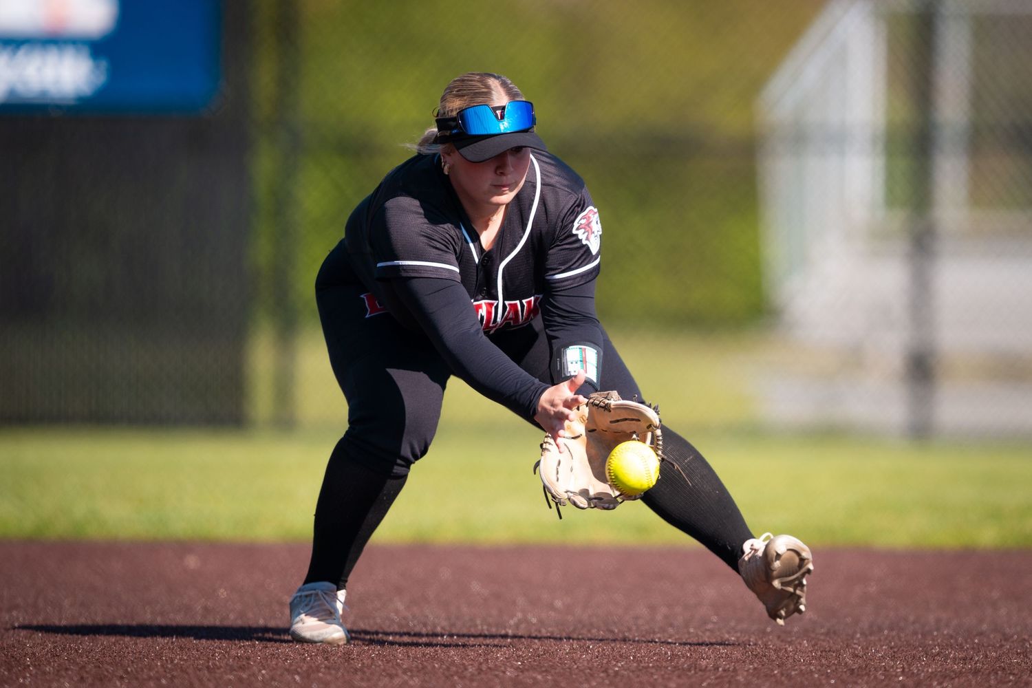 Baseball player in dark uniform crouches low to field a ground ball during infield practice.