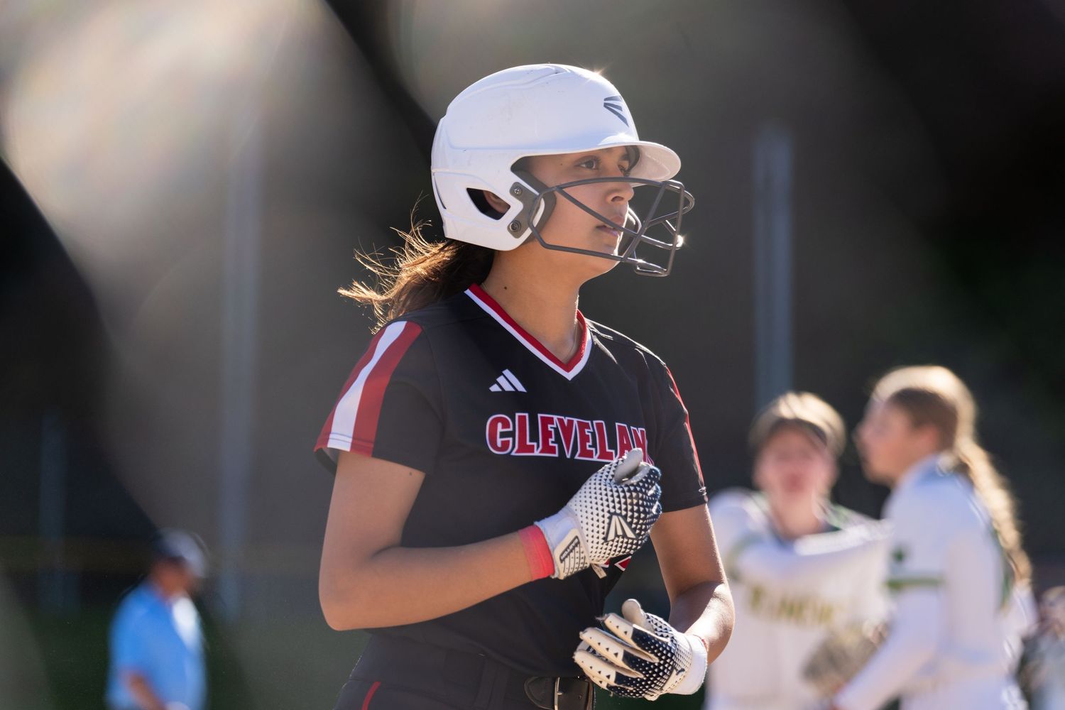 A softball player in a black uniform prepares to bat during a game while wearing a protective helmet.