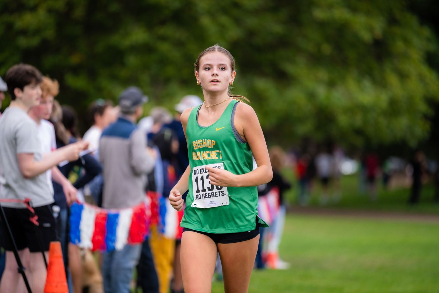 Cross country runners compete in a race through a green park setting during a fall competition.