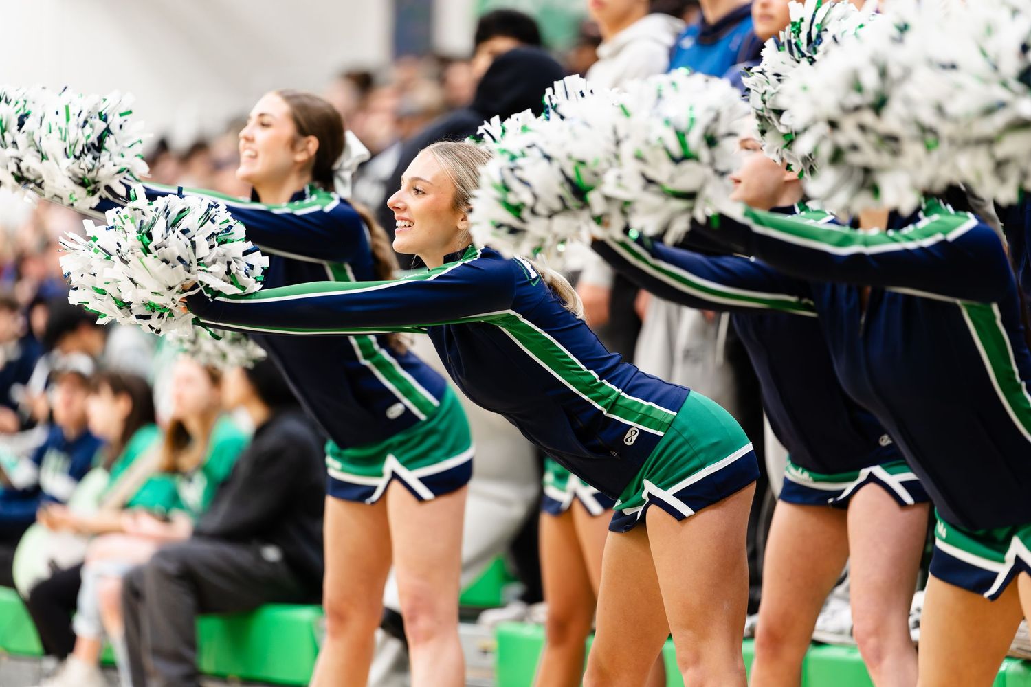 Cheerleaders in green and black uniforms perform synchronized routine during sporting event.