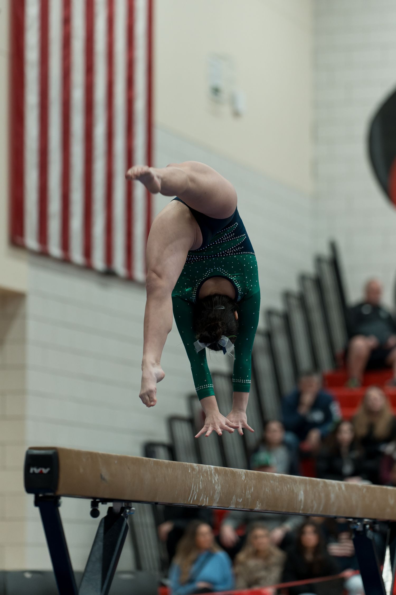 Gymnast performs graceful handstand on balance beam during competitive routine in gymnasium.
