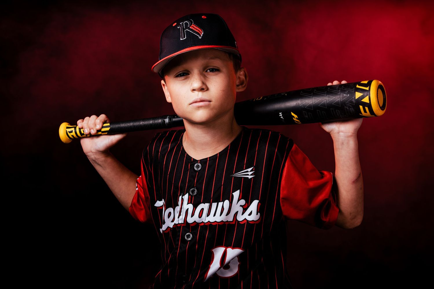 Sports team photo shoot with dramatic red smoke effects and baseball bats against dark background.