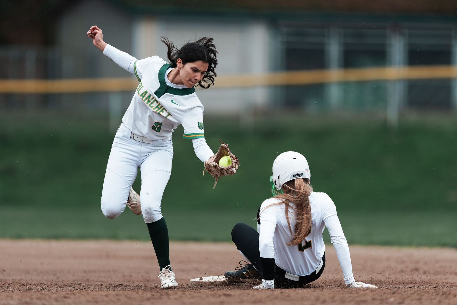 Baseball player slides into base during competitive game while opponent attempts to make the tag.