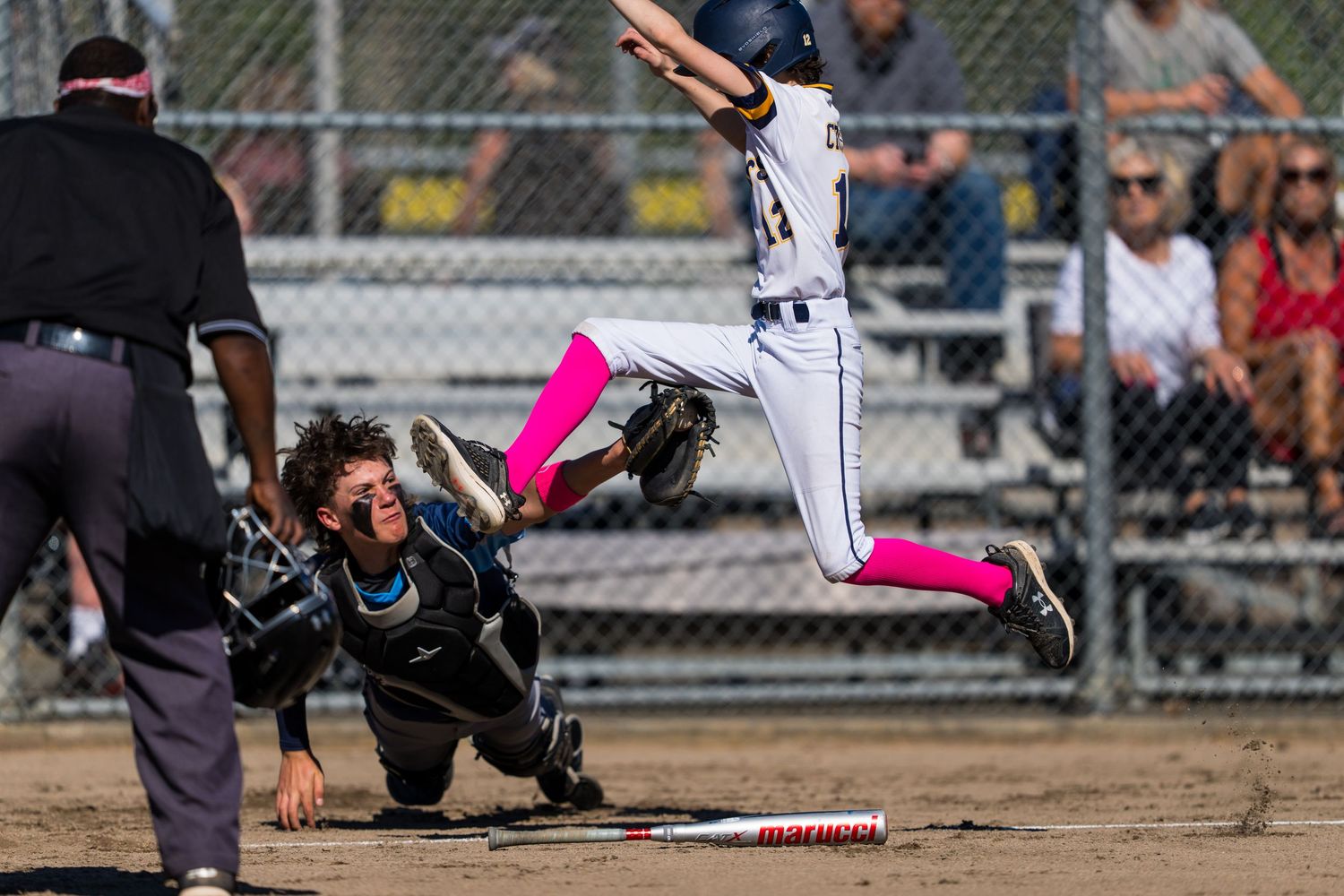 Baseball player in white uniform leaps high at home plate while catcher in black crouches during game action.
