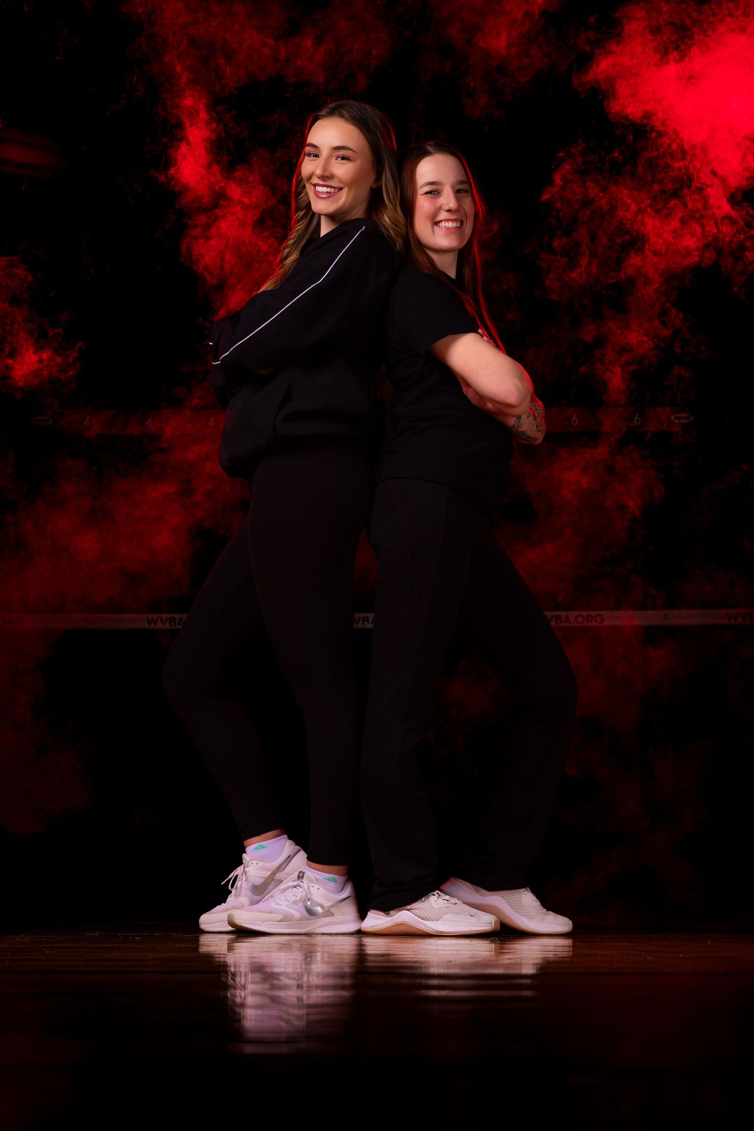 Two dancers in black outfits perform a synchronized dance routine against a dramatic red and black backdrop.