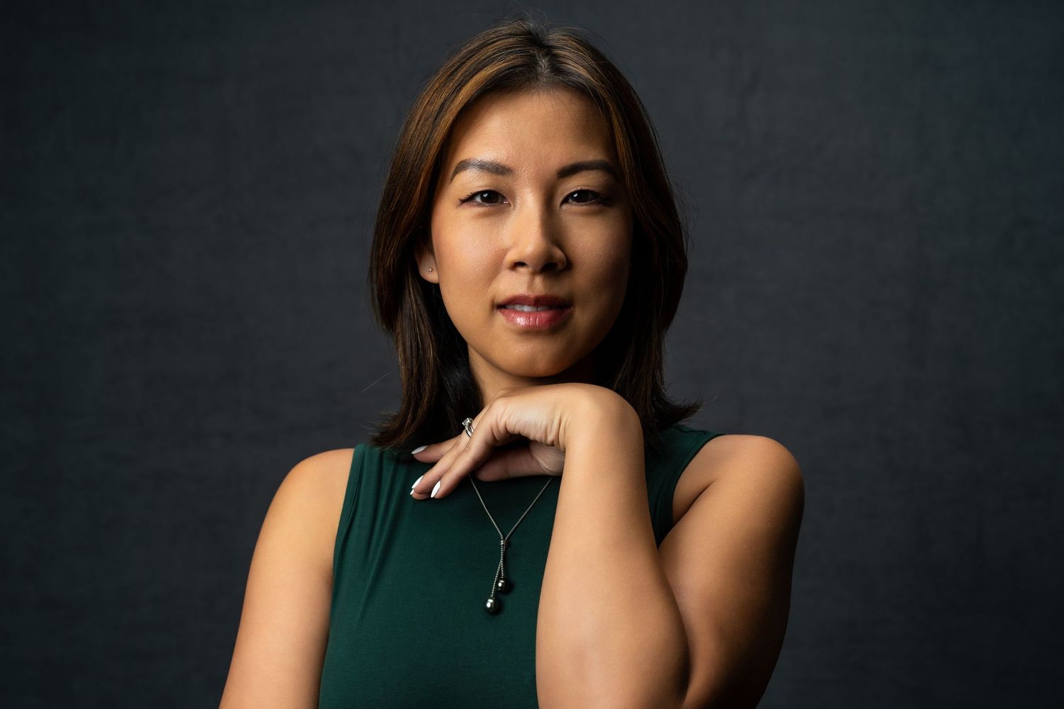 Professional headshot portrait of someone in a dark green sleeveless top against a dark background.