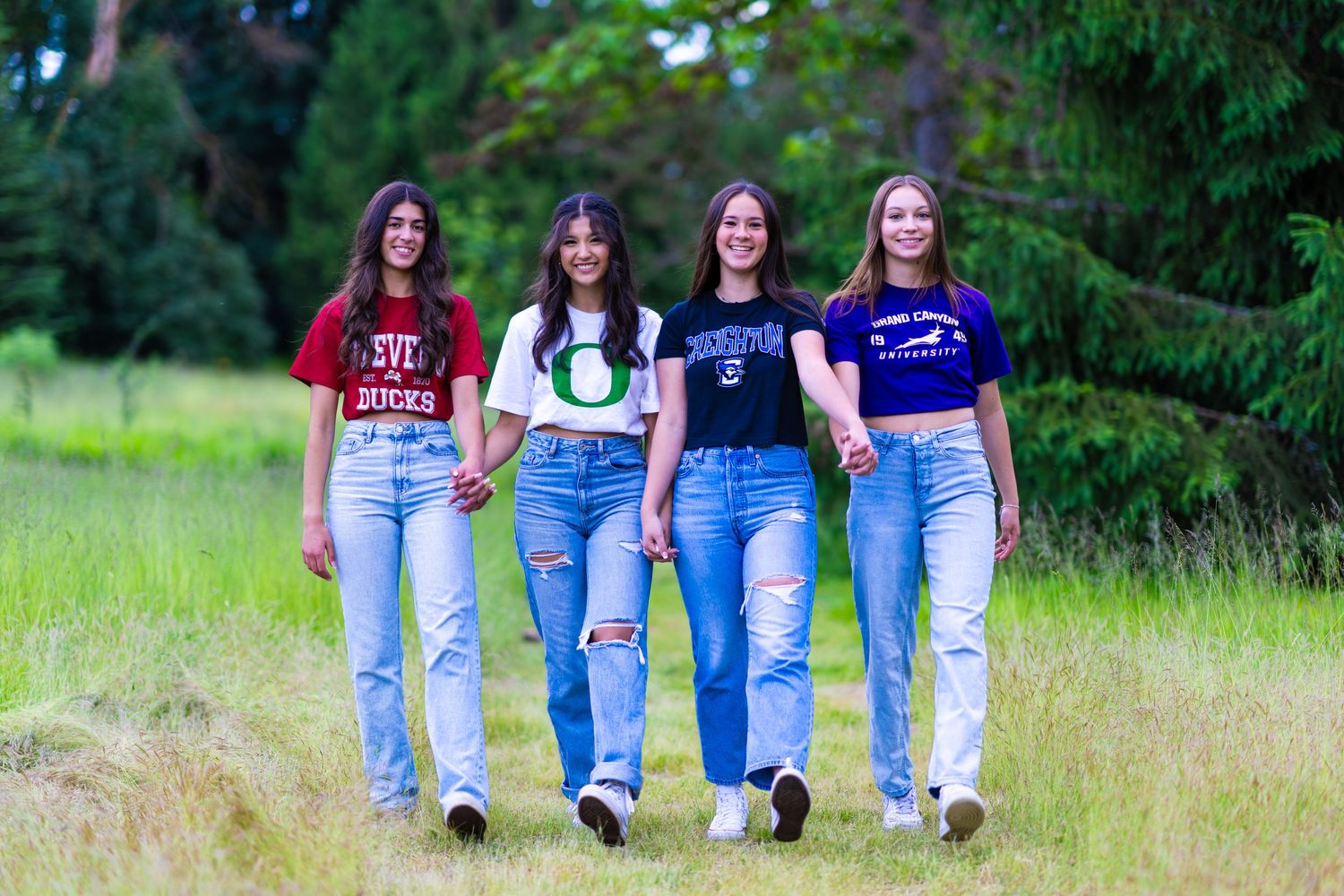 A group of people in blue jeans sitting together on grassy ground outdoors.