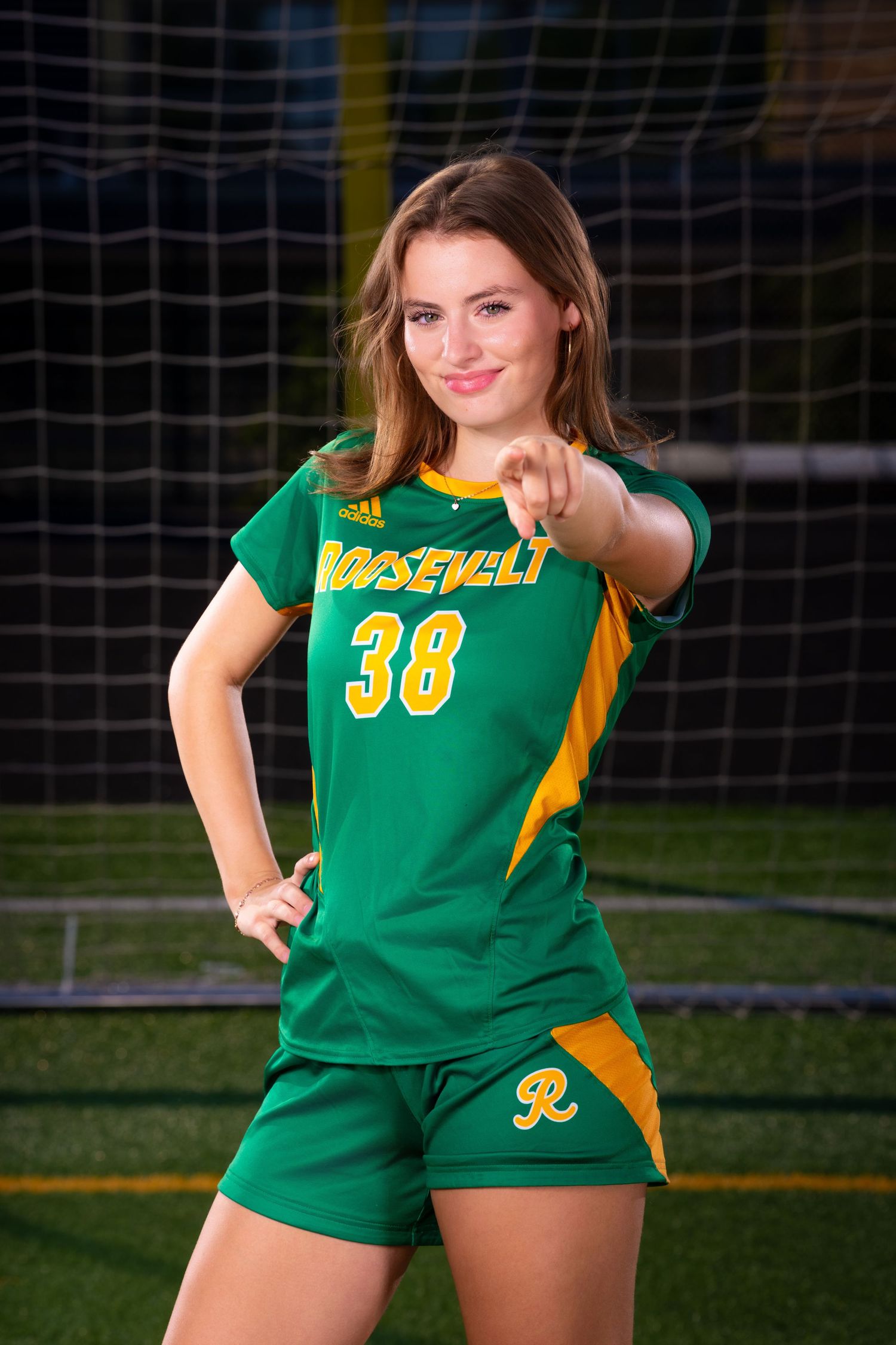Soccer player wearing green and yellow Roosevelt jersey number 38 poses by goal net.