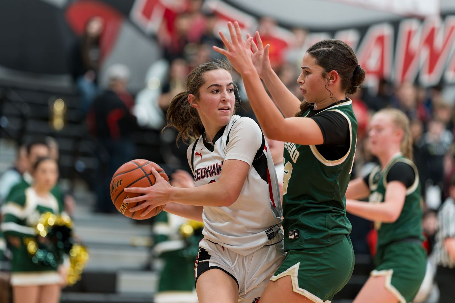 Basketball players compete for possession during an intense game between teams in green and white uniforms.