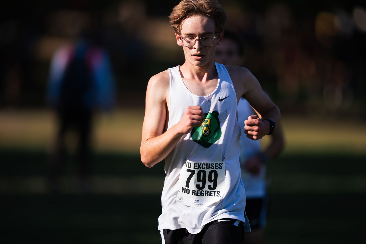 Runner in white tank top holding water bottle during marathon race on sunny day.