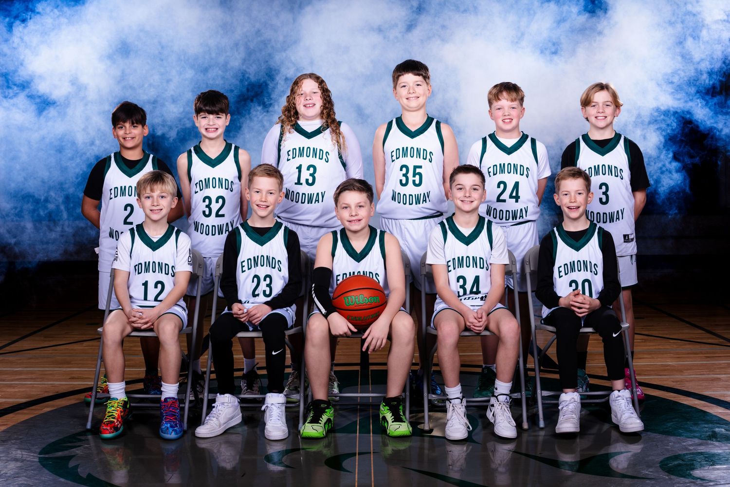 Youth basketball team sits on bench in matching white and navy uniforms during team photo session.