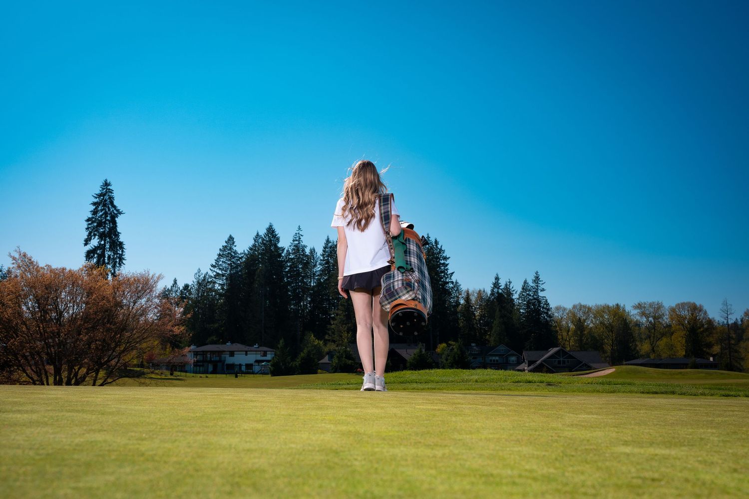 A couple poses together during their engagement photo session in a scenic outdoor setting with blue skies and trees.