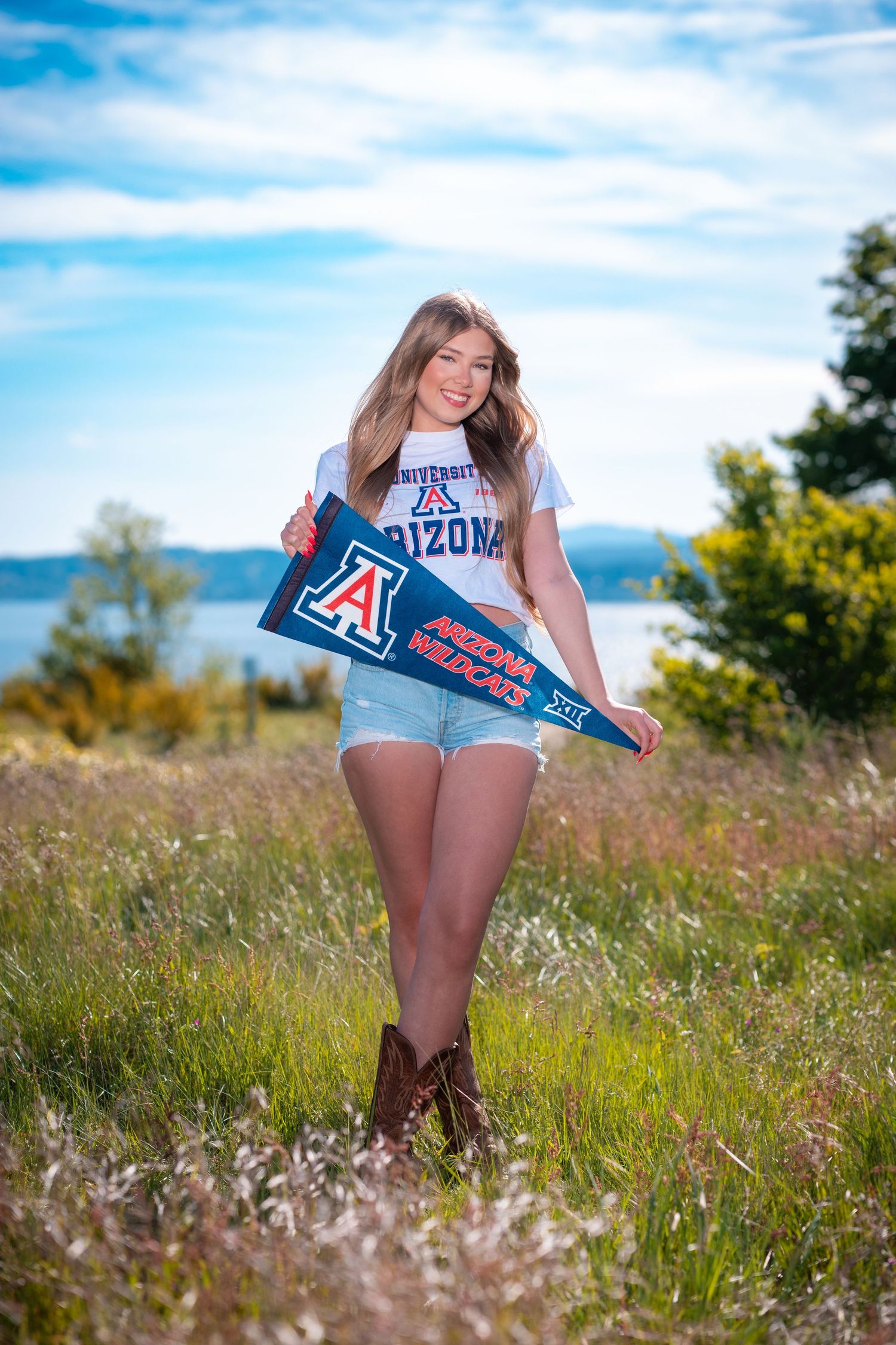 A person in denim shorts poses in a sunny meadow with University of Arizona sports merchandise.