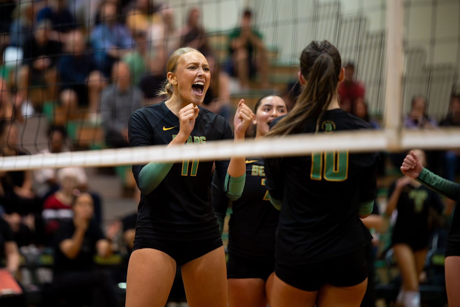 Volleyball players celebrate a point during an intense match in a gymnasium setting.