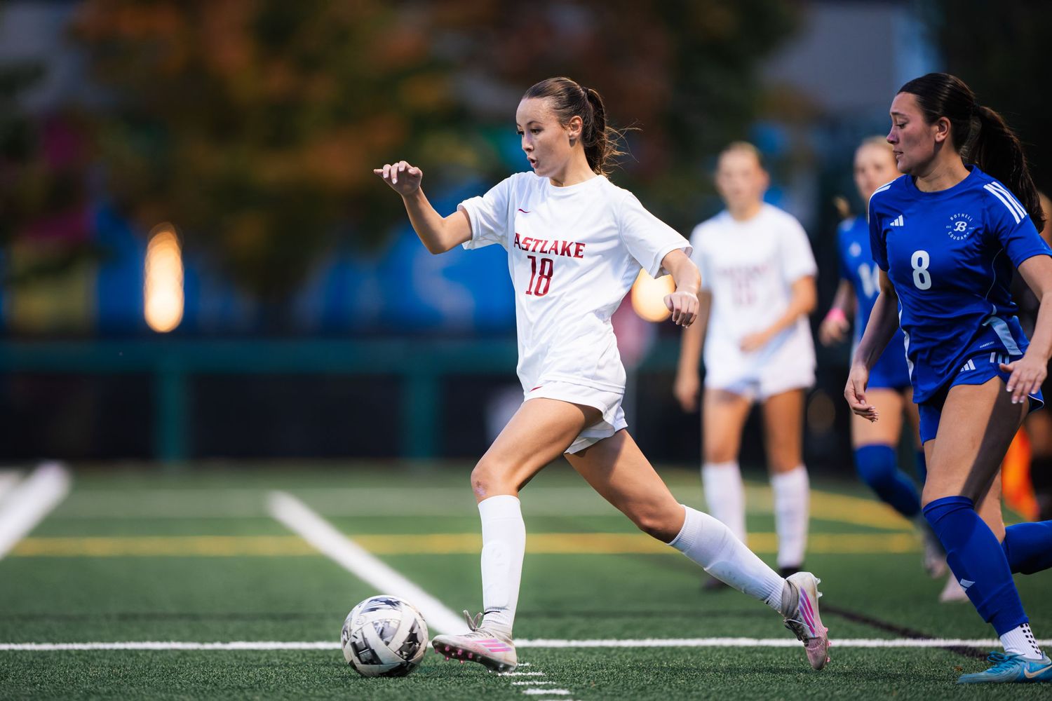 Soccer players compete for possession of the ball during an intense match between teams in white and blue uniforms.