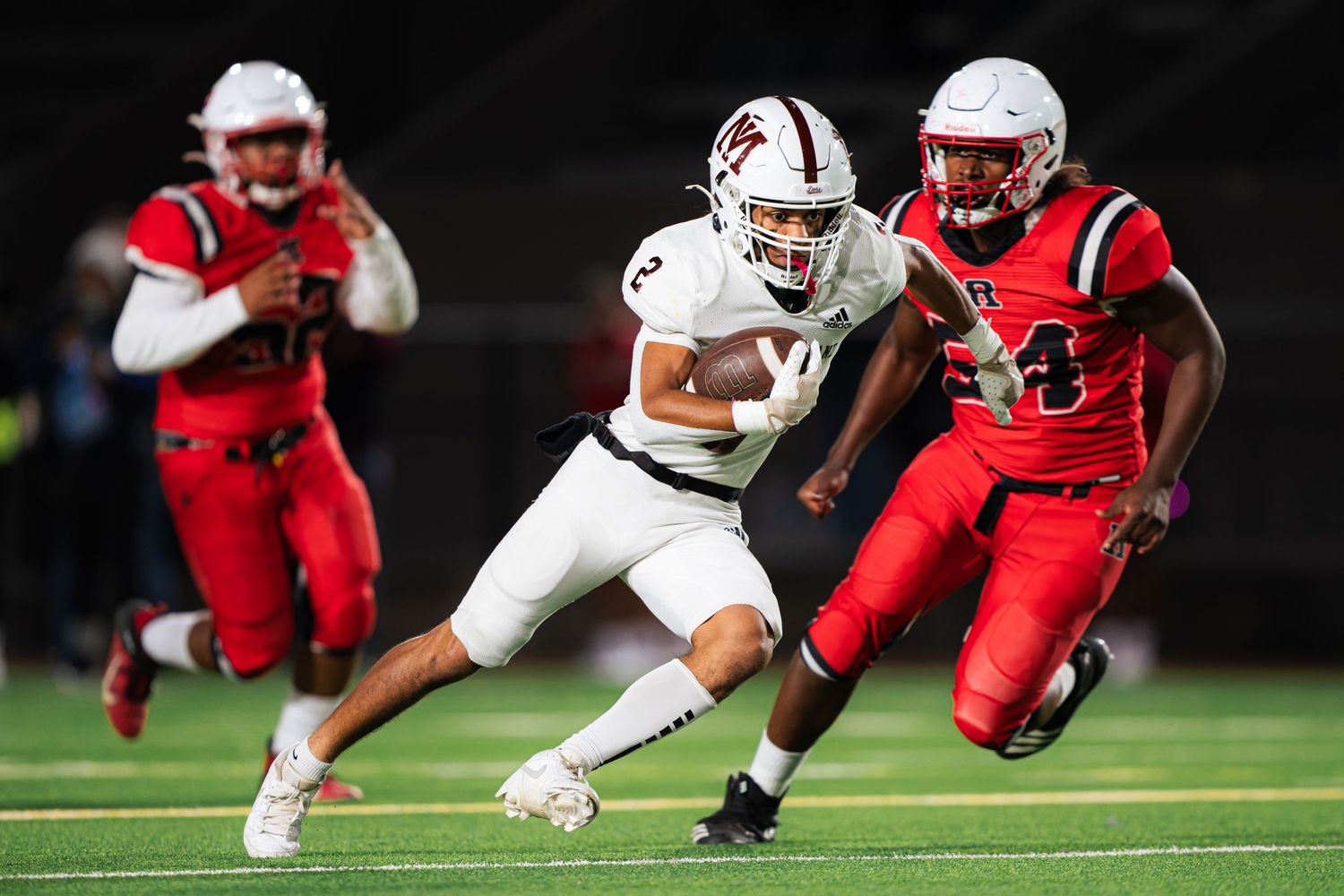 Football players in red and white uniforms compete in an intense tackle during a night game.