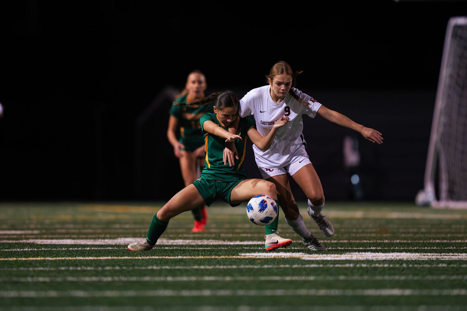 Field hockey players battle for control of the ball during an intense match on artificial turf.