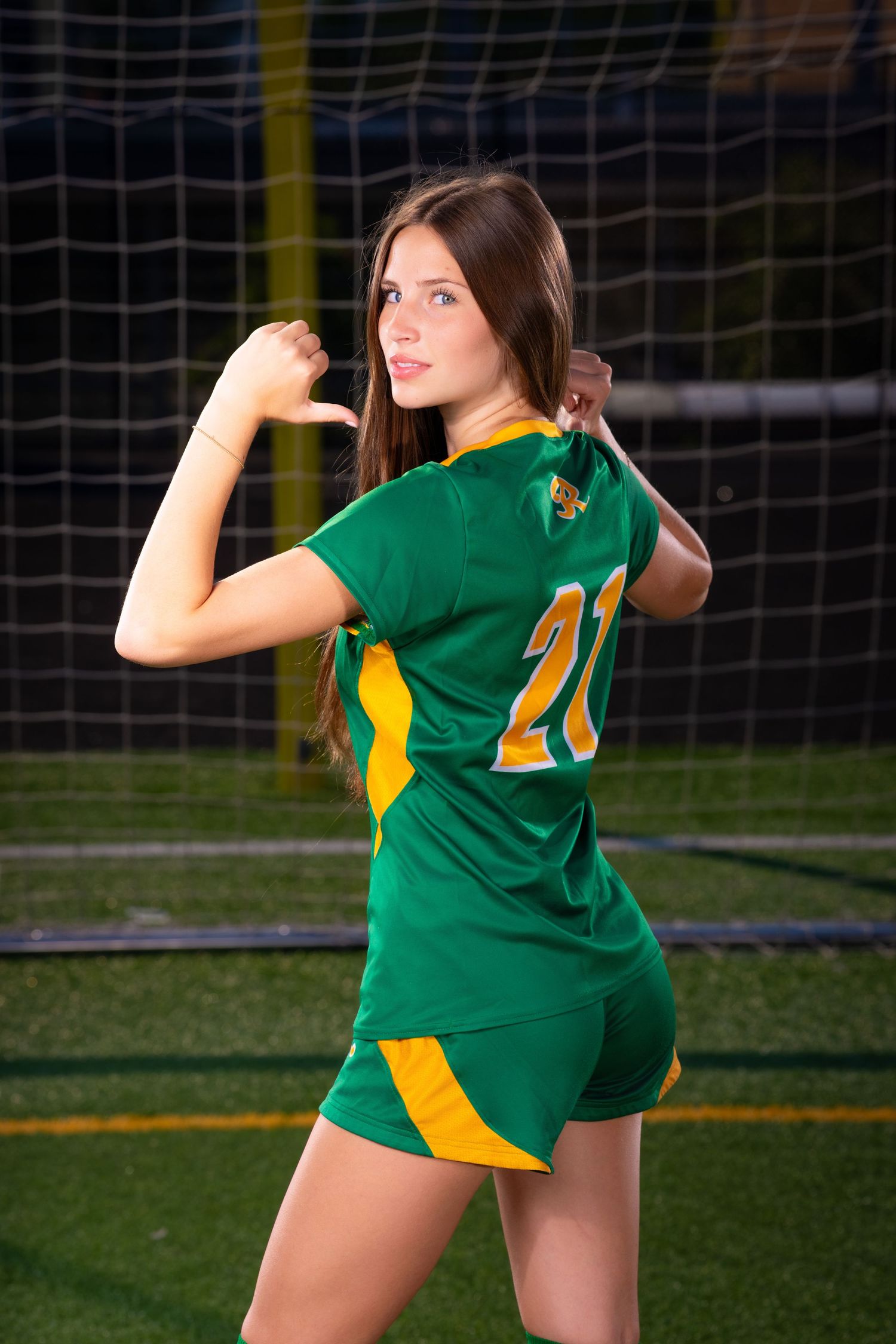 Soccer player in green and yellow uniform performs a throwing motion on the field with goal net in background.