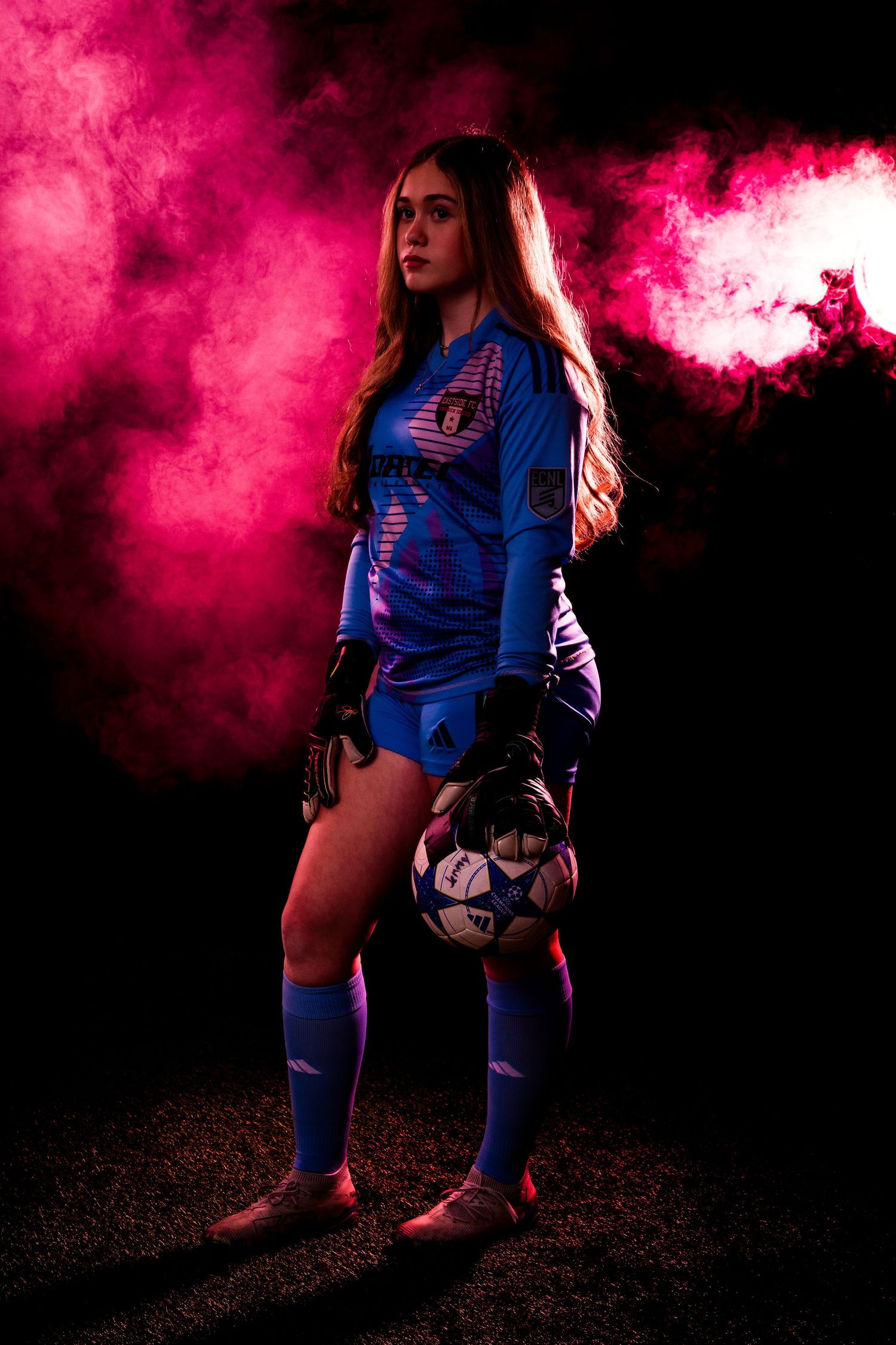 Soccer player in blue uniform against vibrant pink smoke background.