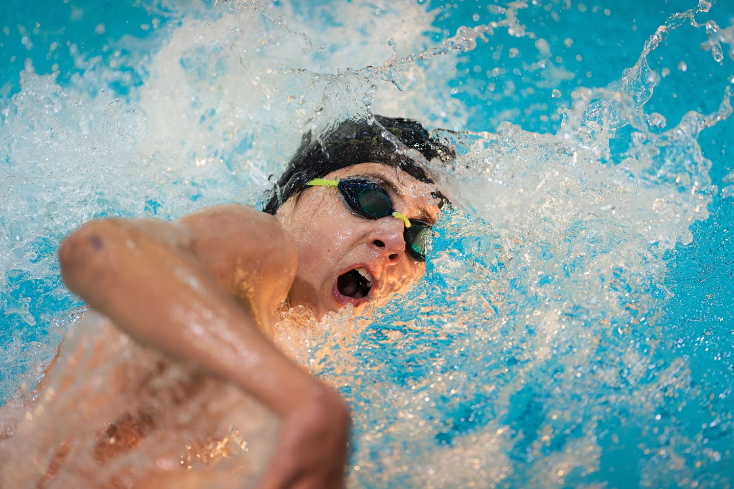 A swimmer performs the butterfly stroke in bright blue pool water during a competitive race.
