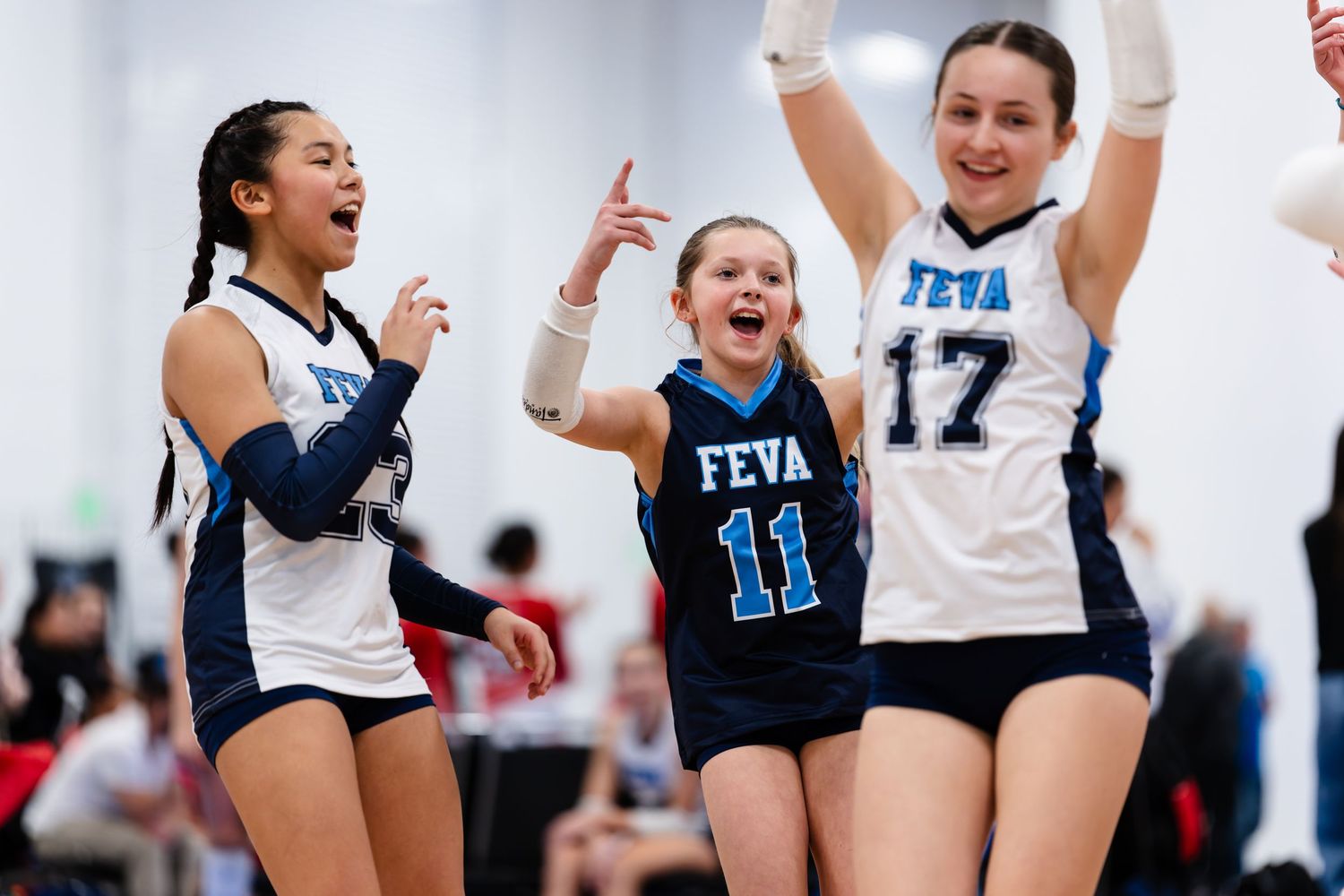 Female volleyball players celebrate enthusiastically during a match wearing white and navy uniforms.