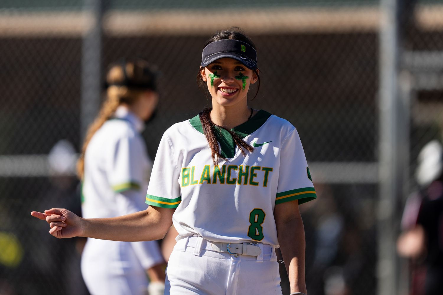 Softball players in green and white uniforms stand on a field during a game.