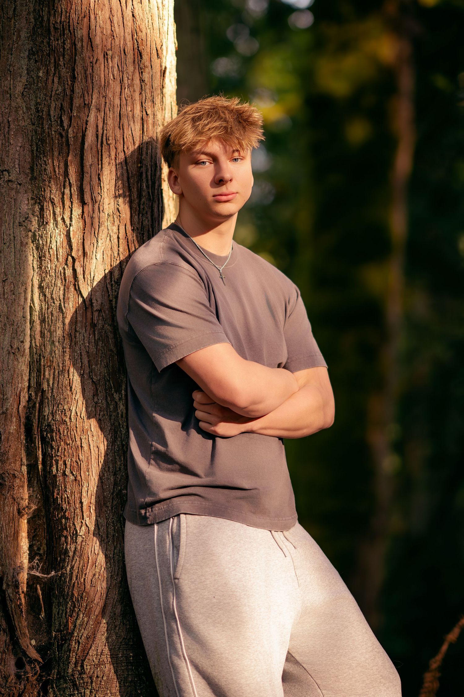 A person in a gray shirt leans against a tree trunk in a series of artistic outdoor portrait poses at sunset.