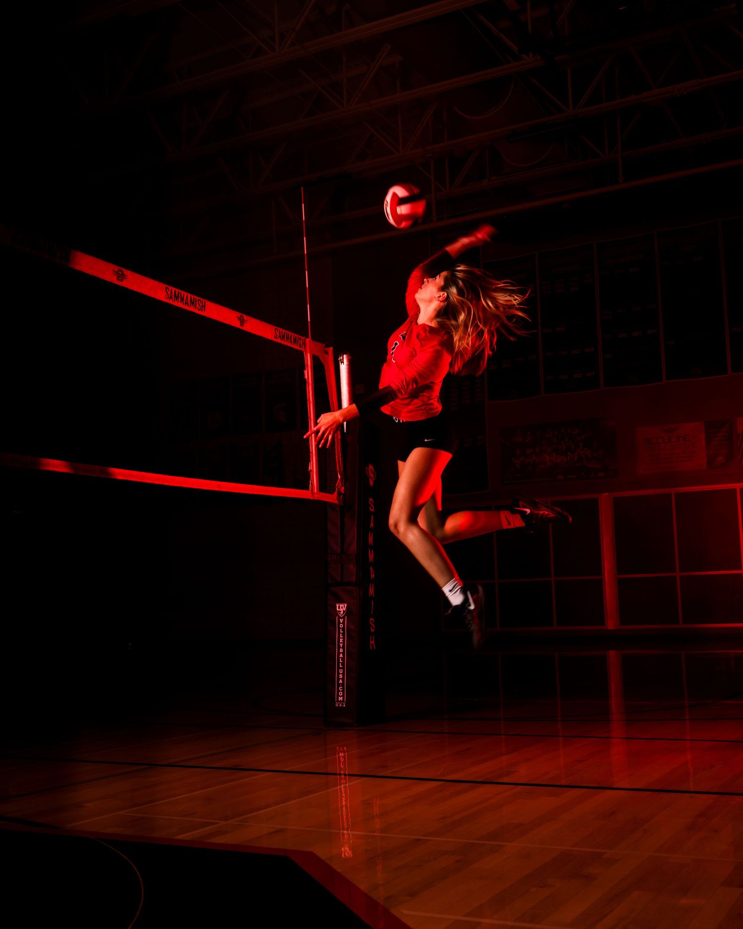 Dancer performs aerial moves in dramatic red lighting on dark stage.