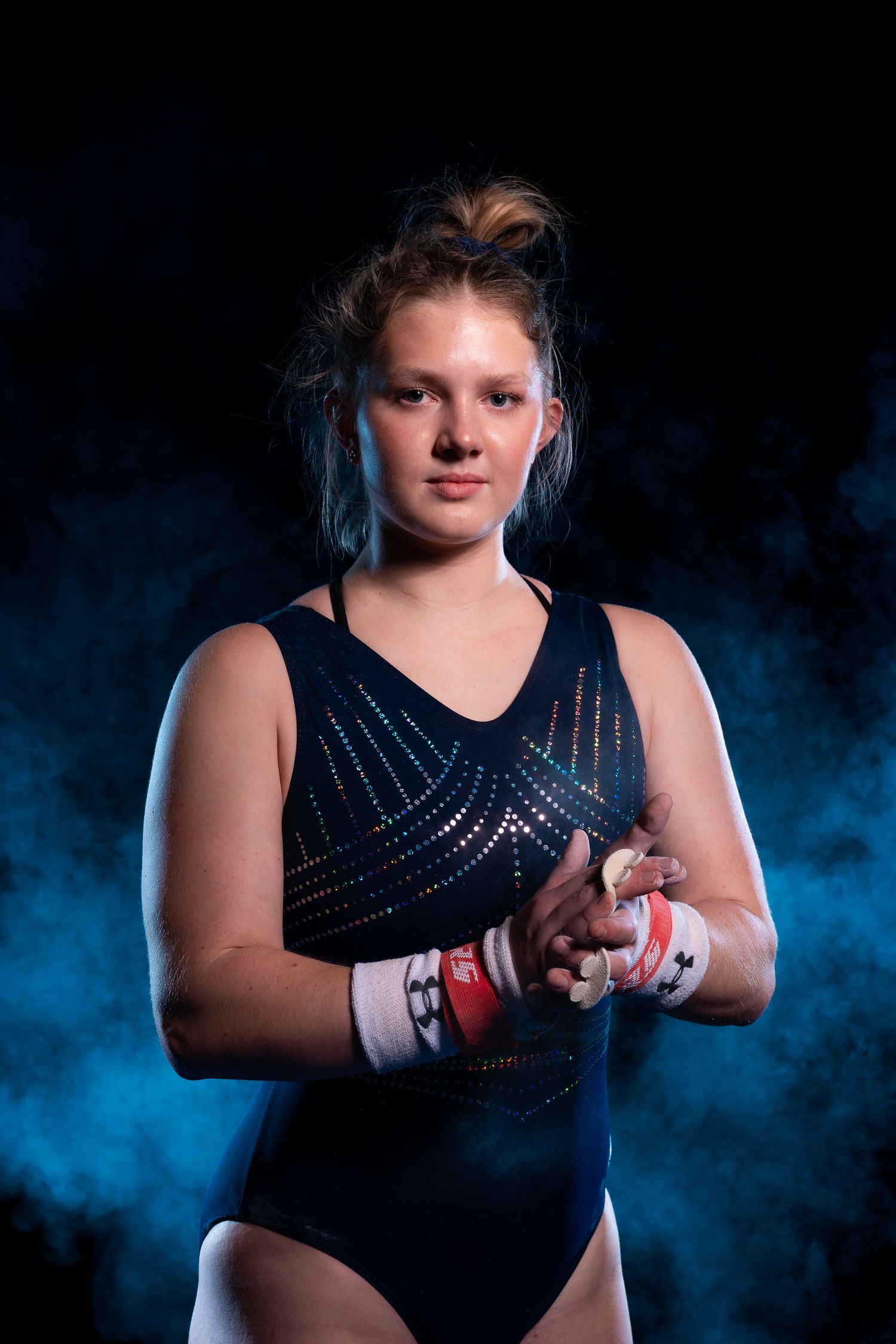 Dramatic portrait series of a gymnast in black leotard against blue smoky background showing different athletic poses.