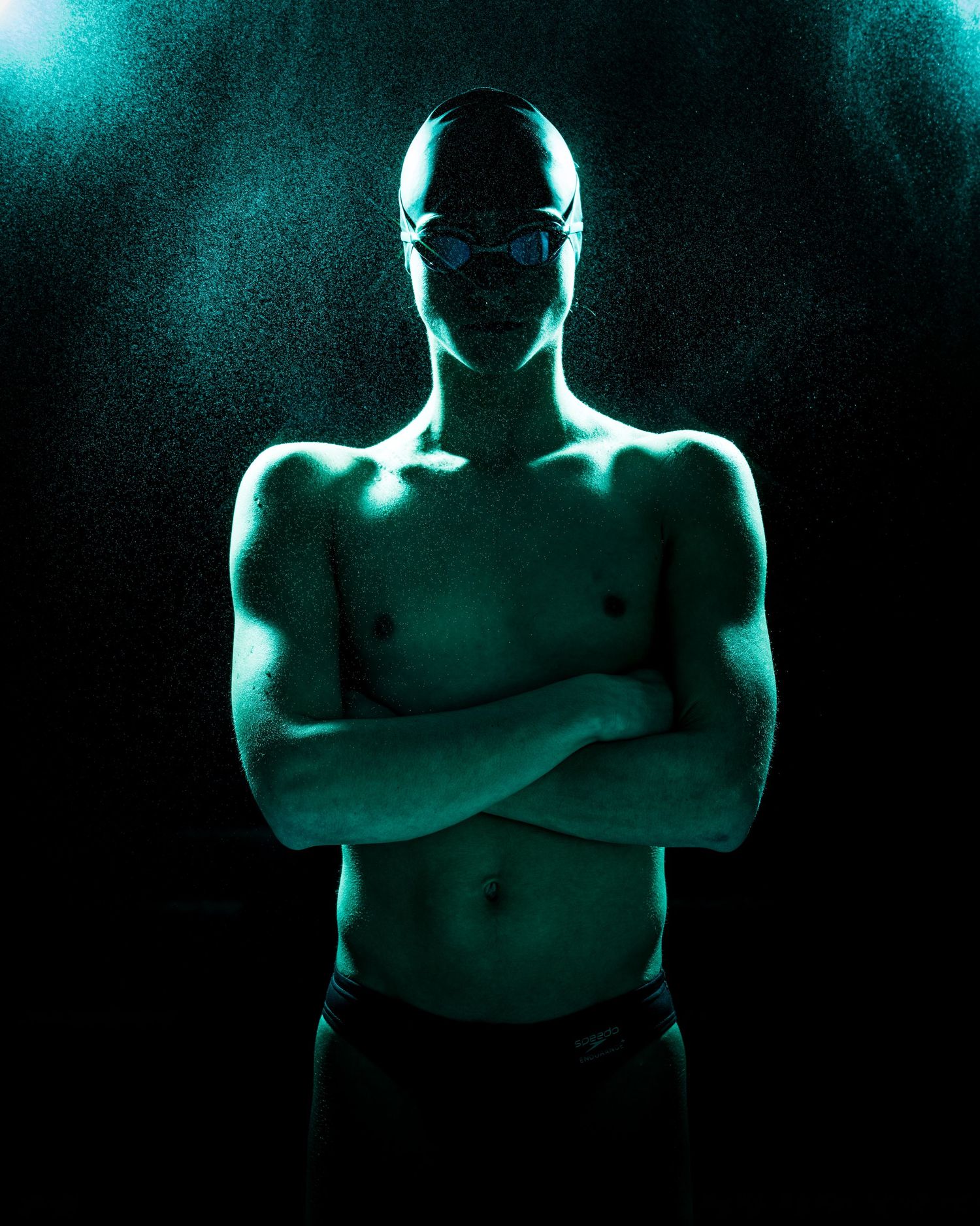Silhouetted figure with crossed arms stands in dramatic turquoise lighting against dark background.