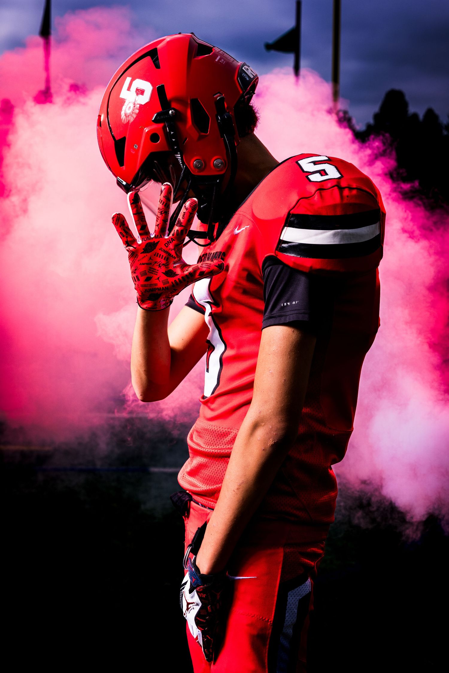 Football player in red uniform stands in dramatic pink smoke during team entrance at night game.