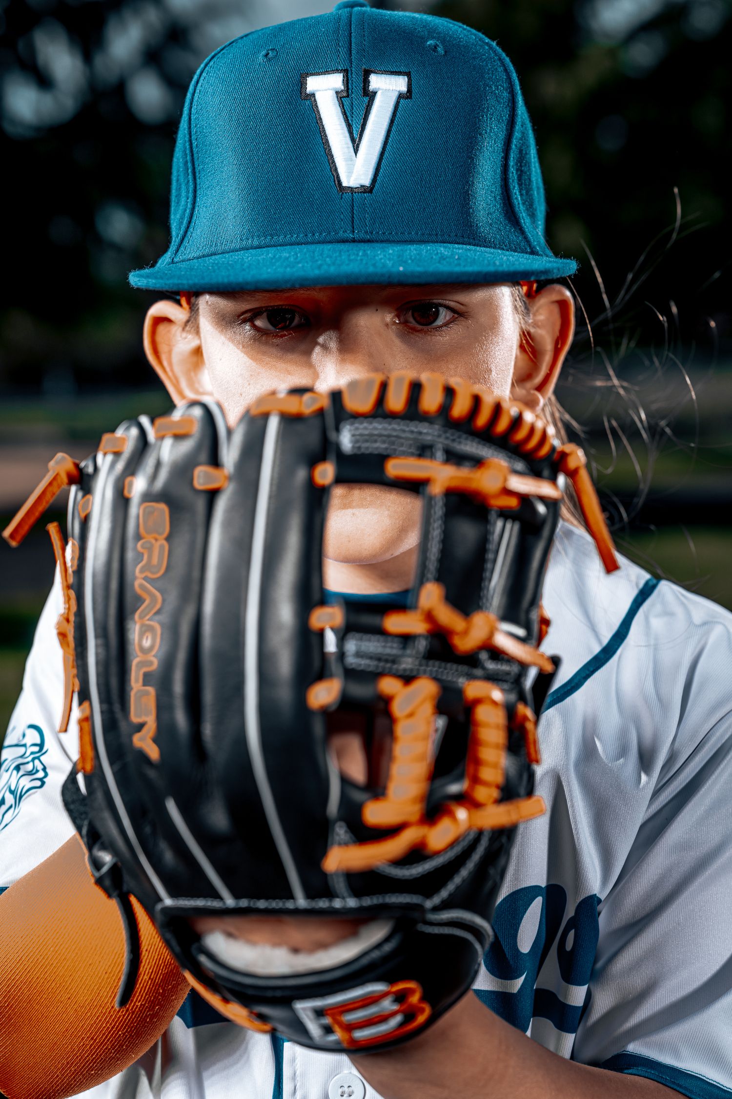 Baseball player in teal cap holds glove up to face showing team logo.