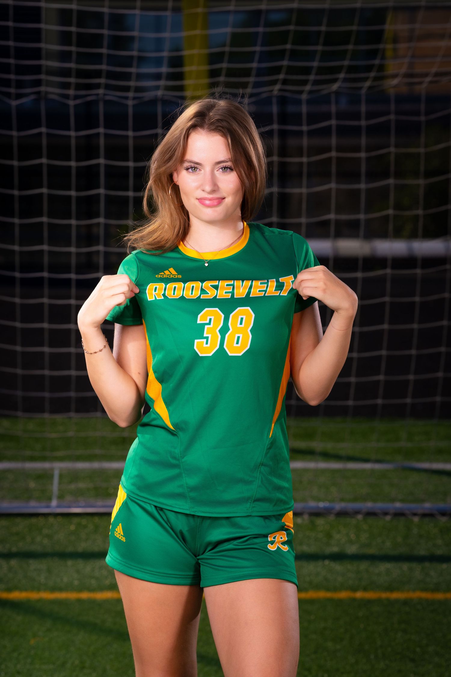 Athletic uniform in green and yellow colors displayed on grass field with goal net visible in background.