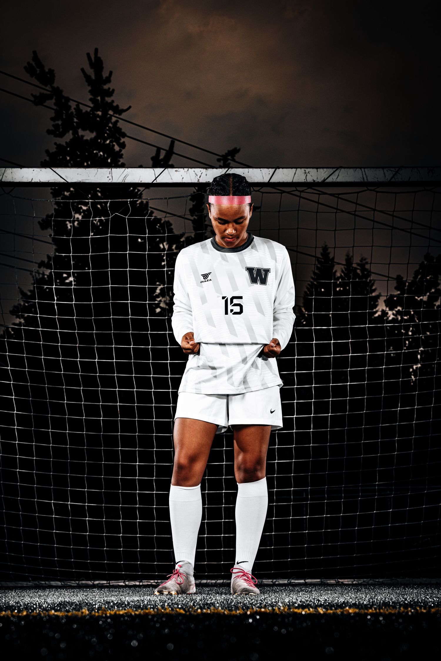 Soccer player in white uniform stands in dramatic lighting against goal net.