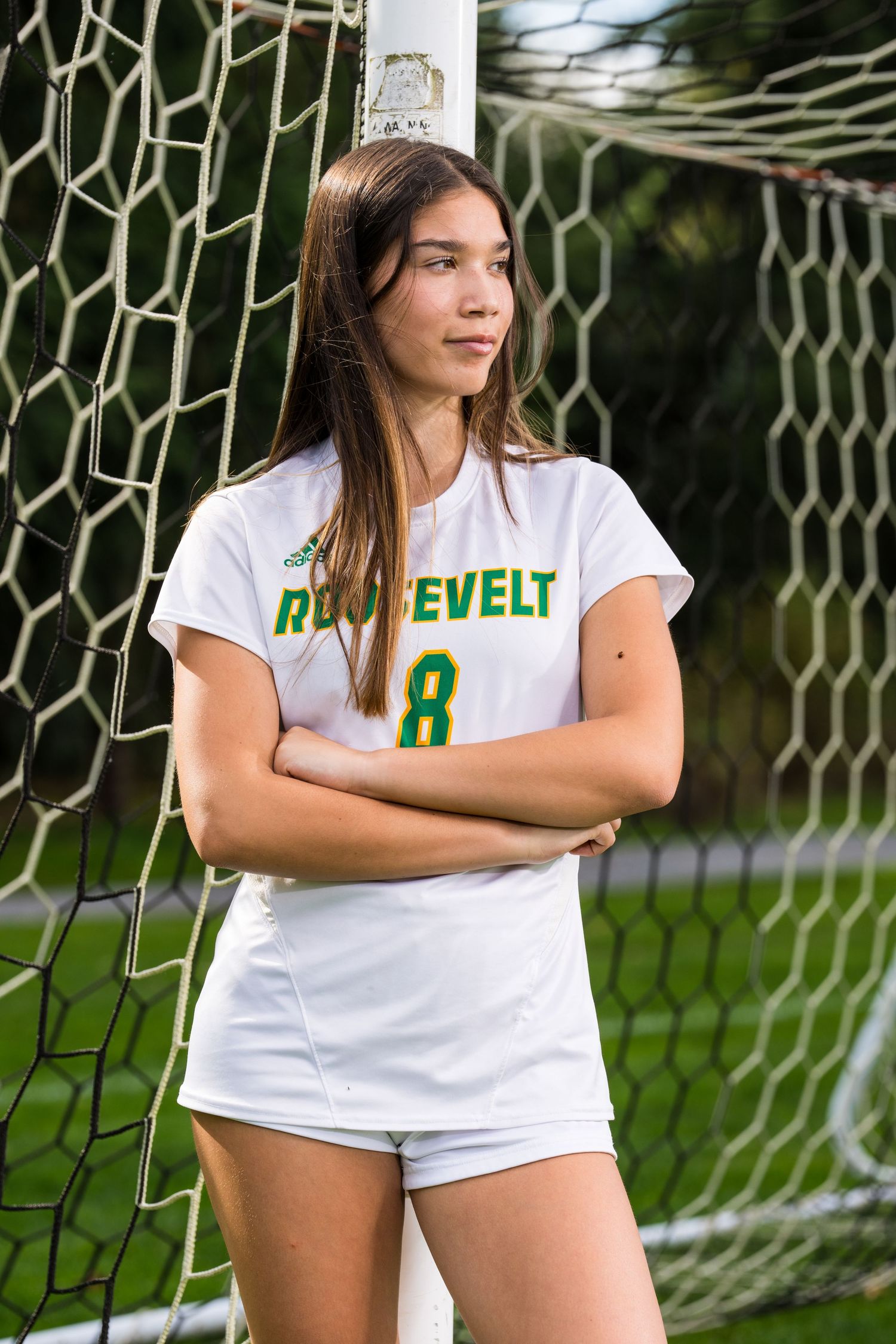 Soccer player in white uniform poses near goal net during outdoor sports photoshoot.