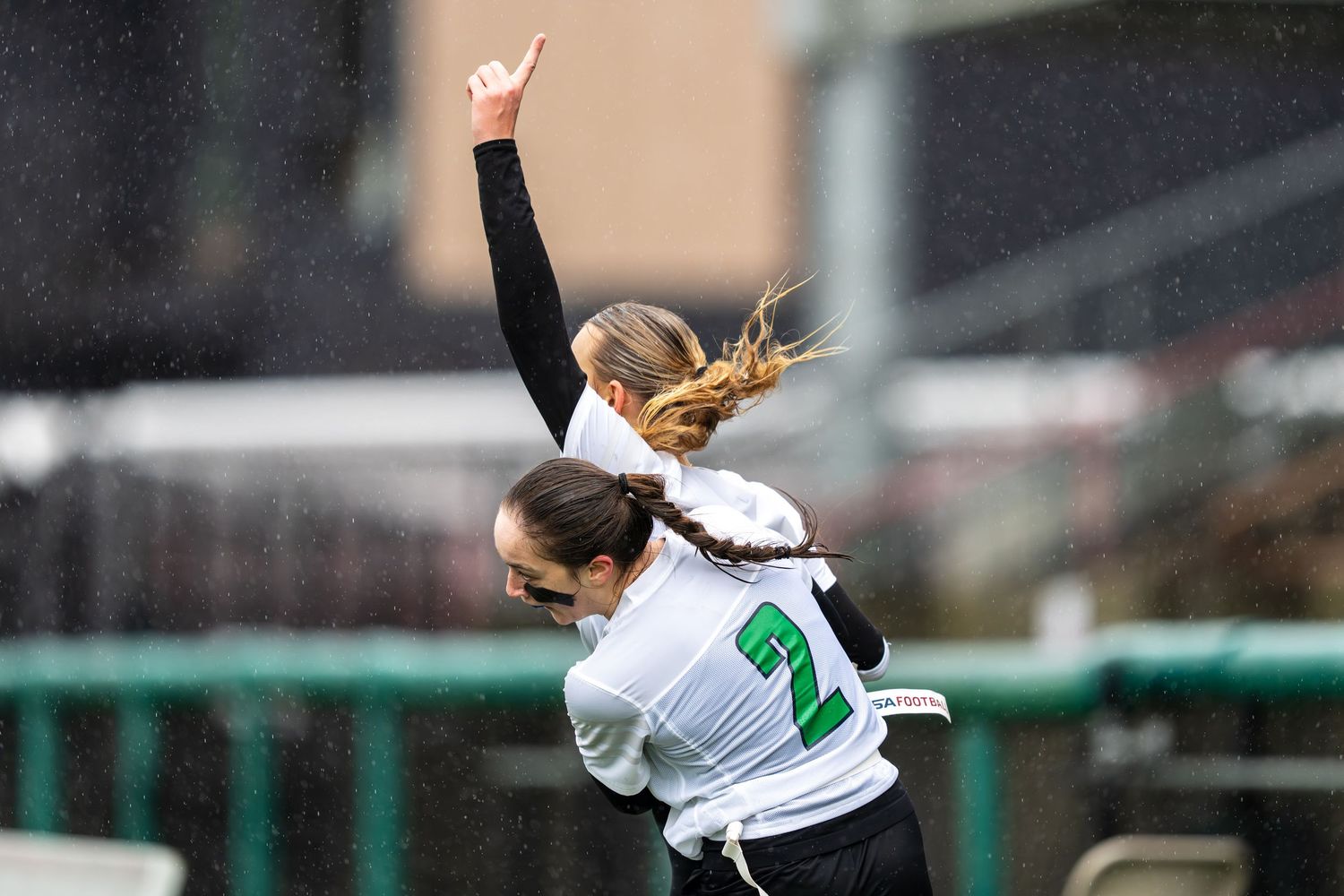 Soccer player in white jersey number 21 celebrates with raised arm and ponytail flying during match.