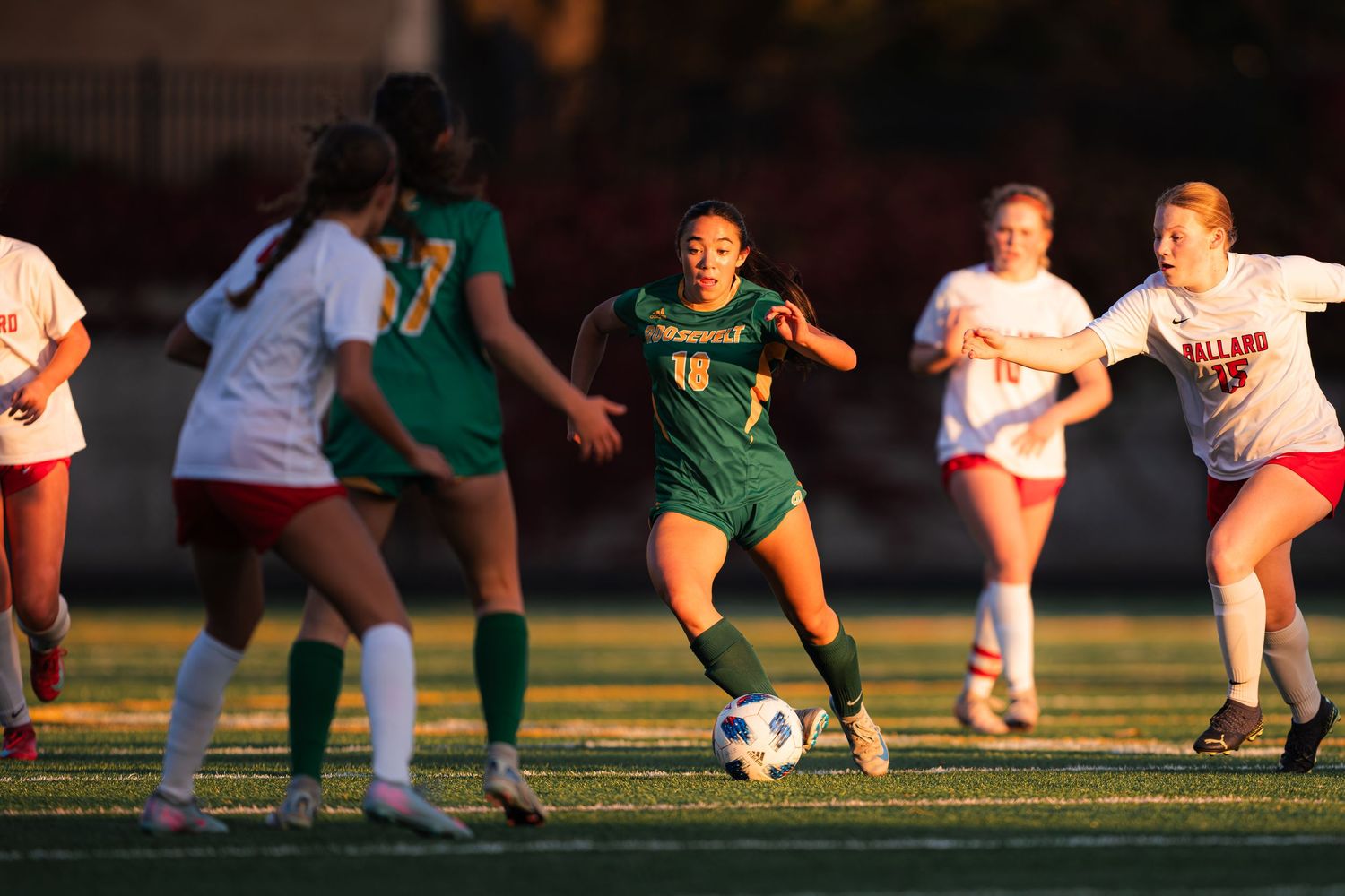 Soccer players kneeling on a field during golden hour with long shadows cast across the grass.