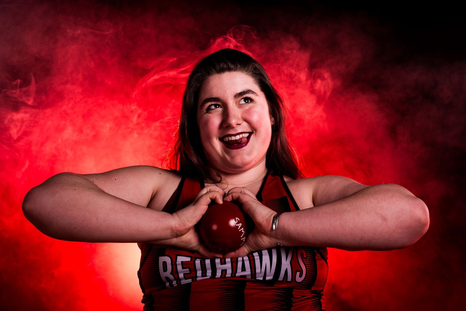 A person in a Redhawks jersey poses enthusiastically against a dramatic red-lit background.