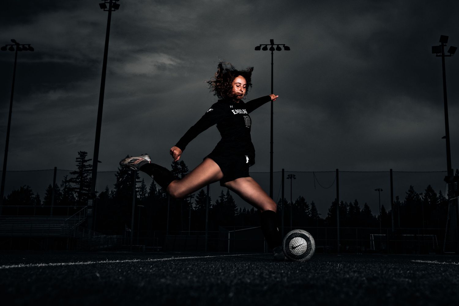 A sequence of silhouetted soccer players kicking a ball against a dramatic dark sky with stadium lights.