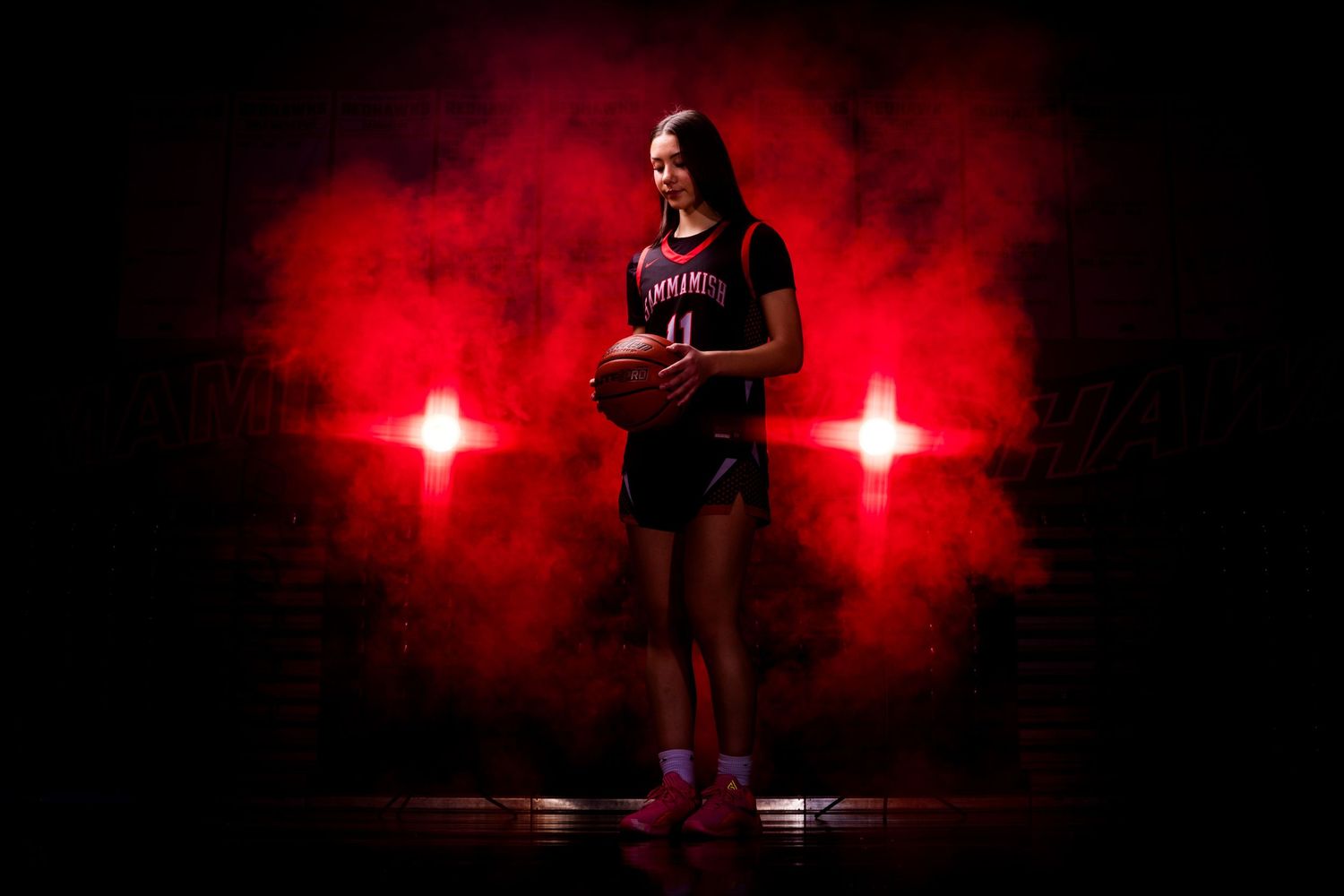 Basketball player performing athletic moves in dramatic red lighting and smoke effects.