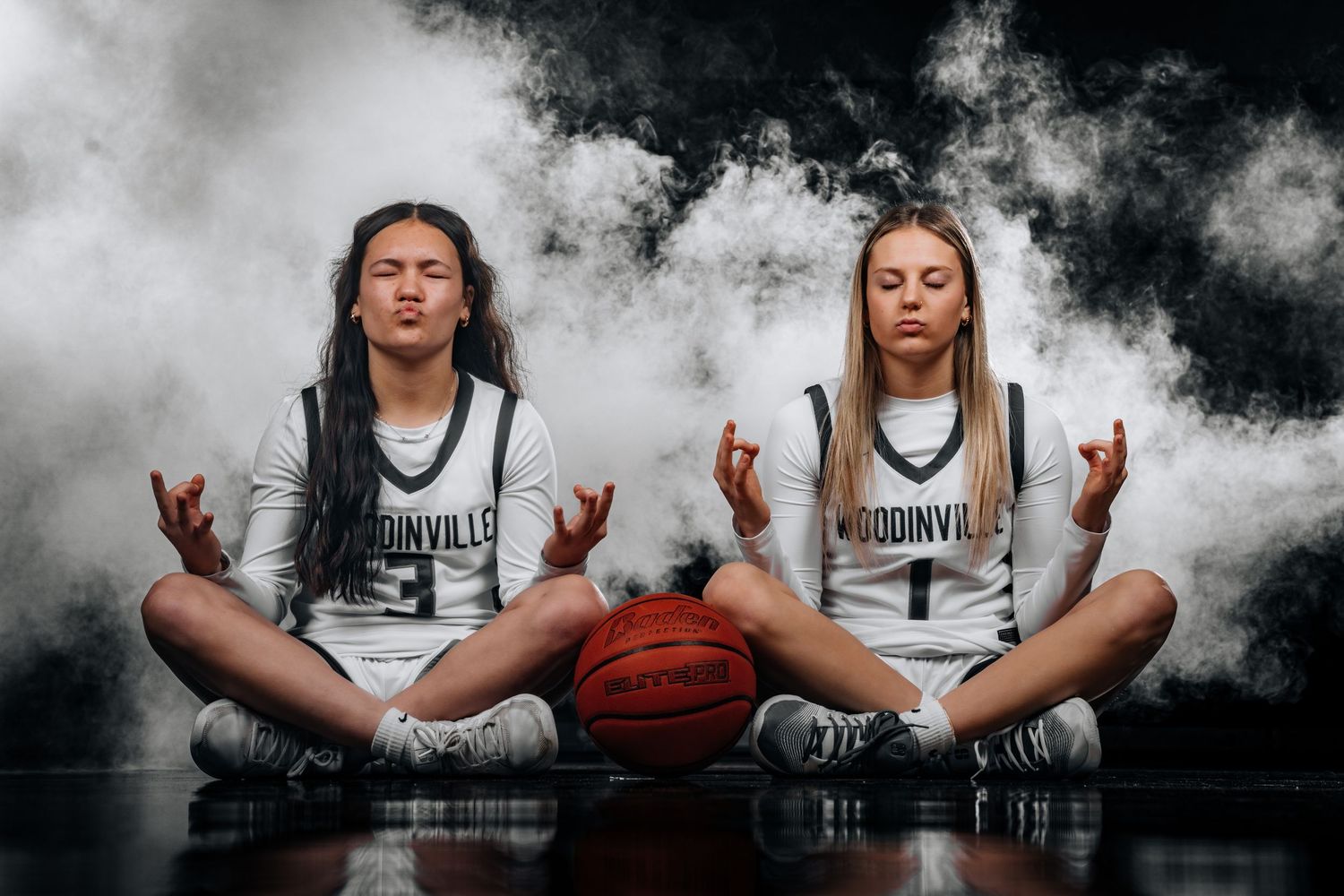 Basketball player in white jersey meditates with basketball in dramatic black and white composition.