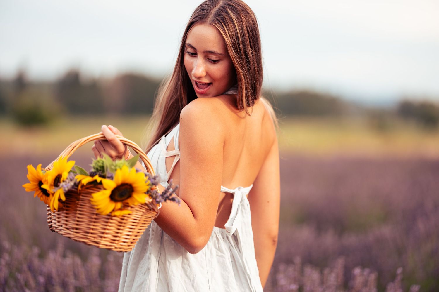 A female graduating senior holds a sunflower basket in a lavendar field during a senior portrait session shot by Carlos Sanchez Photography