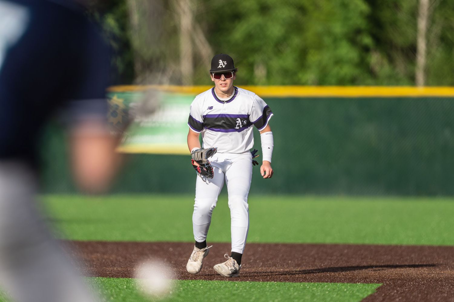Baseball player in white uniform delivers a pitch from the mound during a game on a sunny day.