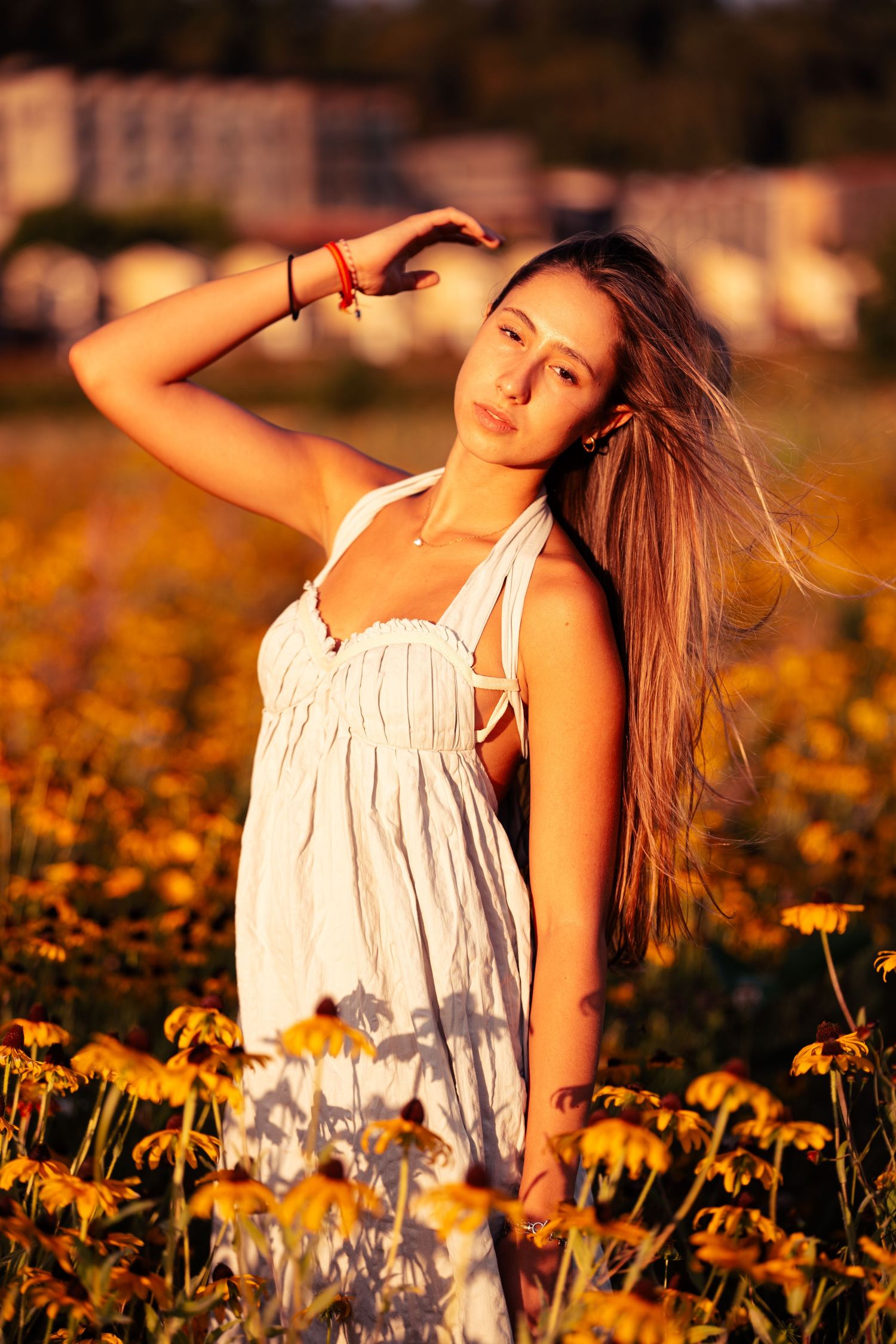 Person in white dress posing in a field of yellow wildflowers at golden hour.