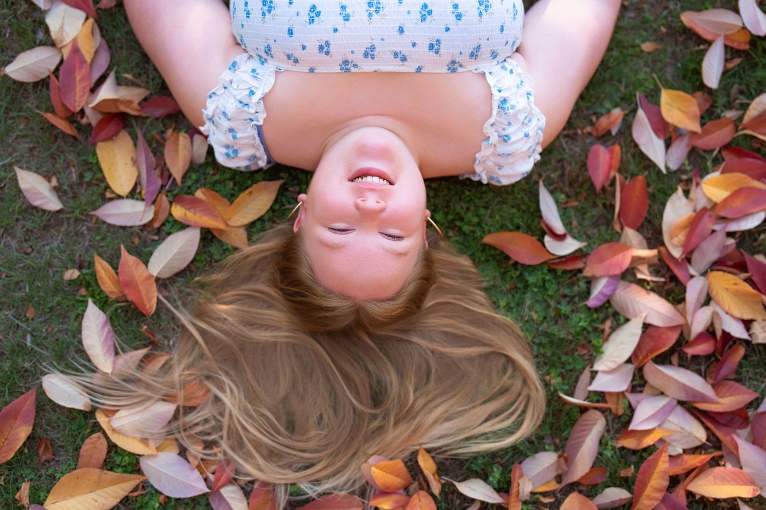 Person lying in colorful autumn leaves during outdoor photoshoot.