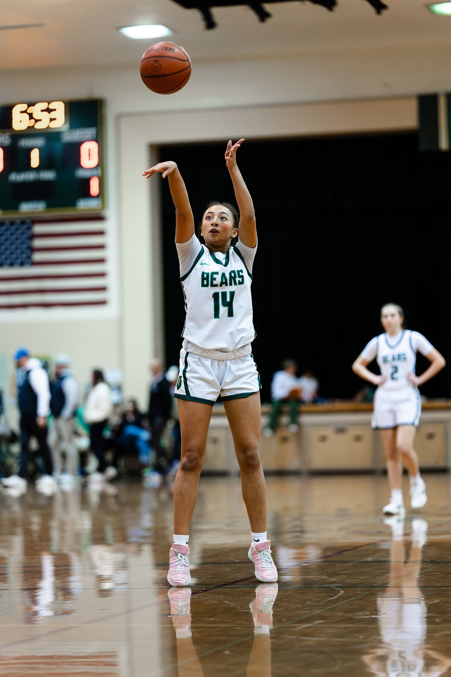 Basketball player in white Bears jersey number 14 shoots the ball during a game with scoreboard and American flag visible.