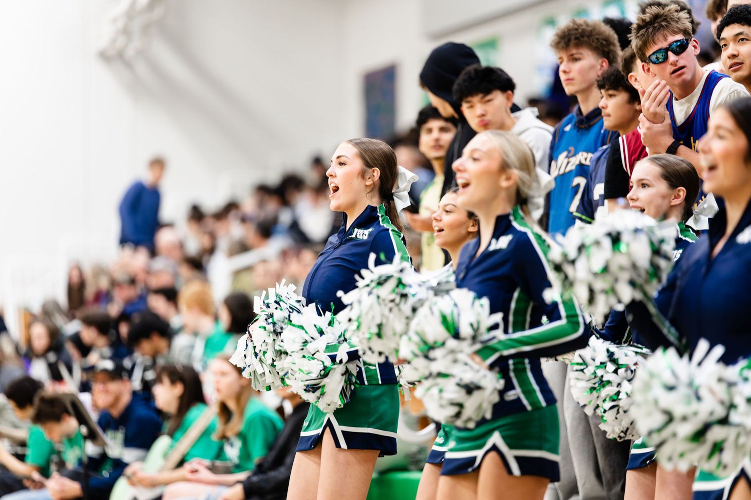 Cheerleaders in blue and white uniforms perform with pom poms during a high school sports event in a gymnasium.